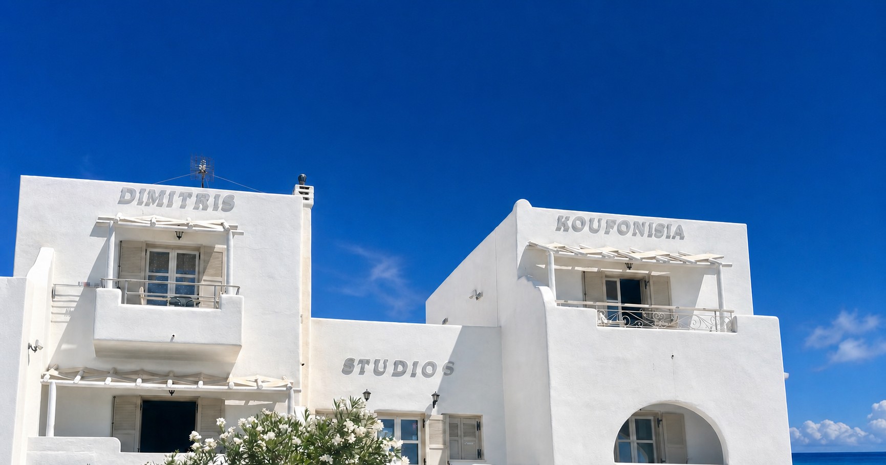 Λευκή κυκλαδίτικη πρόσοψη του Dimitris Studios κάτω από βαθύ μπλε ουρανό